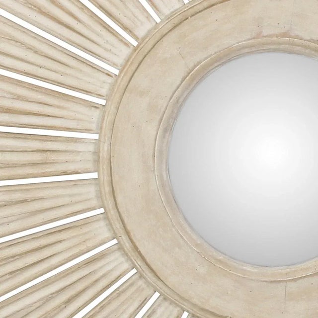 A large painted white sunburst mirror with varying lengths of rays connecting to a center molded ring. The mirror is...
