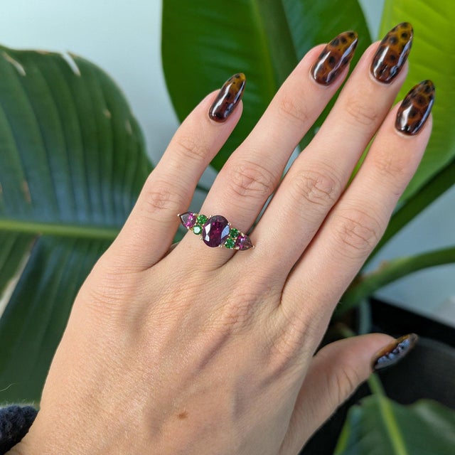 A 2.96-carat oval purple garnet glows in a rich grape-purple at the center of this solid 14K yellow gold ring, flanked by...