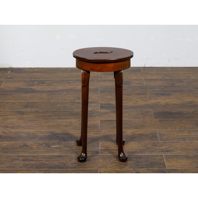An English walnut stool from the 19th century with oval seat and central hand-cut handle. This charming 19th-century...