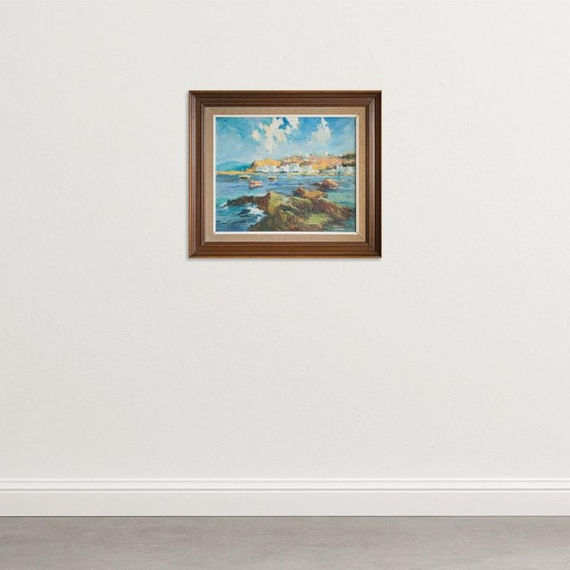 This signed oil on canvas depicts the picturesque harbour at P ort of Llança on the Costa Brava, capturing the sunlit...