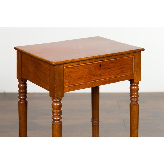 A petite English walnut side table from the early 19th century, with single drawer, turned legs and casters. Created in...