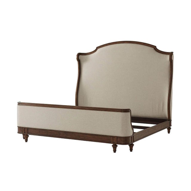 A French carved california king size bed with an arched and molded upholstered headboard with scroll wings, an upholstered...