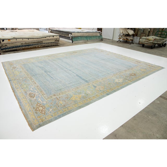 This hand-knotted wool rug features a light blue background with yellow and beige accents in a framed design. This rug...