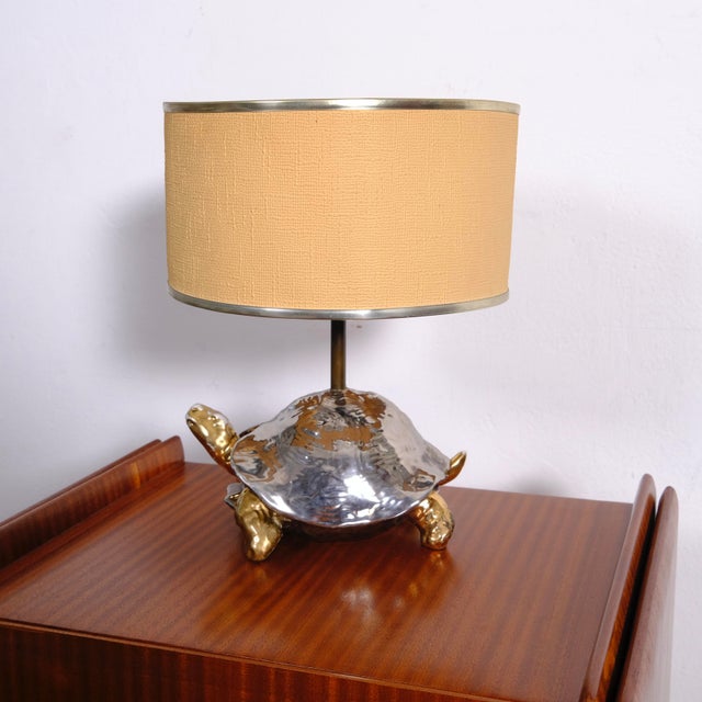 Lamp with white ceramic sculpture painted silver and gold. Chrome-plated brass rod. Oval fabric lampshade with two gold-...