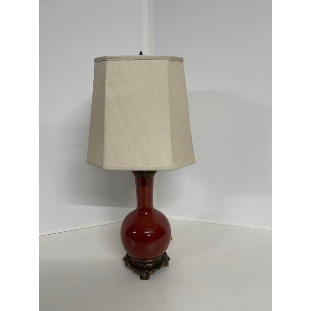A classically designed ginger jar-style table lamp with a glossy oxblood red or deep burgundy glazed ceramic base in a...