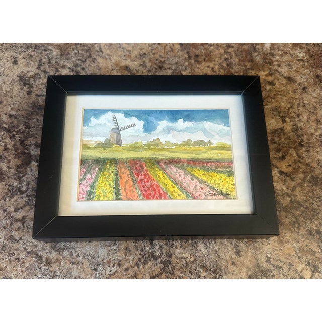 This original watercolor depicts a serene countryside scene with vibrant, blooming fields leading toward a distant...