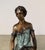 Refined figural bronze sculpture depicting a seated woman holding a vessel, rendered in a style inspired by classical...