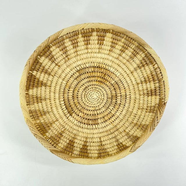 Beautiful handwoven basket bowl crafted from natural plant fibers in warm earth-tone hues. The shallow coiled form and...