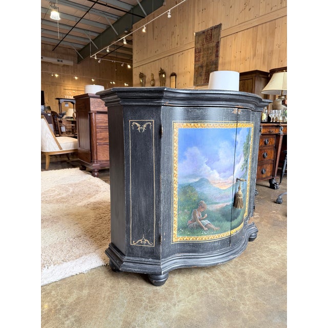 Vintage curved front cabinet finished in distressed black with a hand painted scenic panel across the doors. The painting...