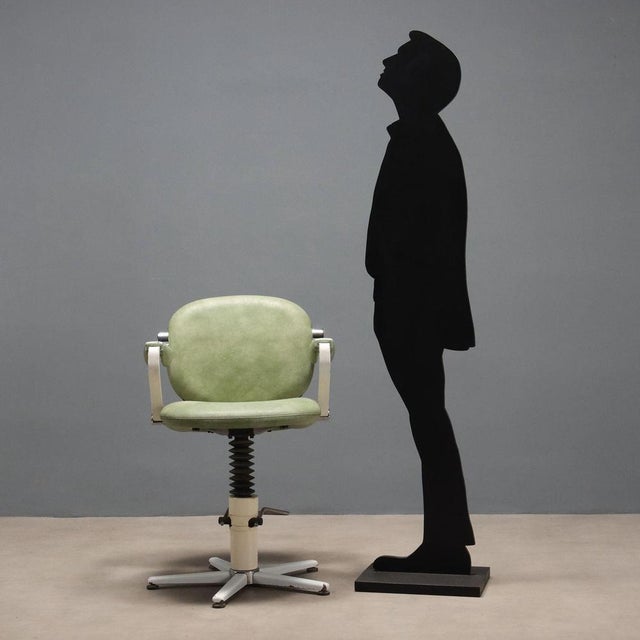 Vintage barber chair, swivel and height-adjustable, with enameled metal base, seat upholstered in green skai. This piece...