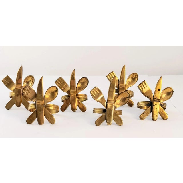 This set includes six vintage brass napkin rings featuring a charming utensil design, showcasing a fork, knife, and spoon....