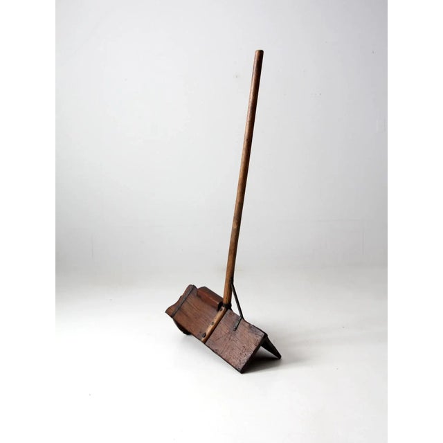 Antique primitive farm tool with a long wooden pole handle and an angled shovel-like bucket base. The hand-hewn...
