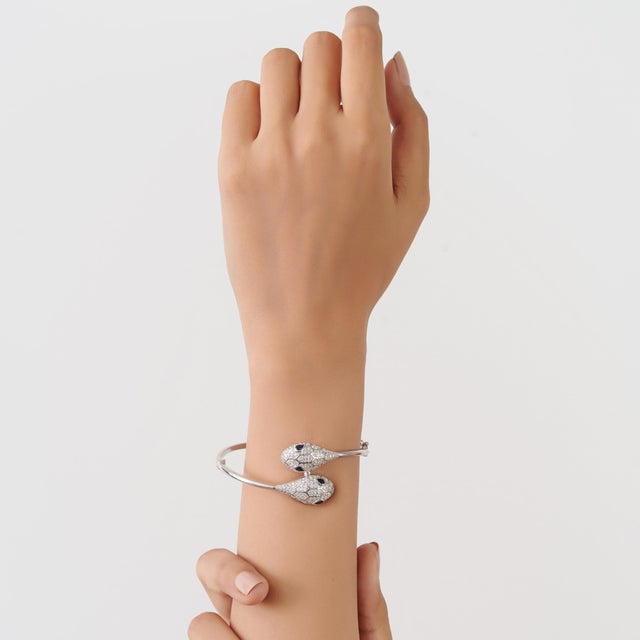 This double-headed serpentine bangle bracelet is crafted in 925 sterling silver and features two sculpted serpent heads...
