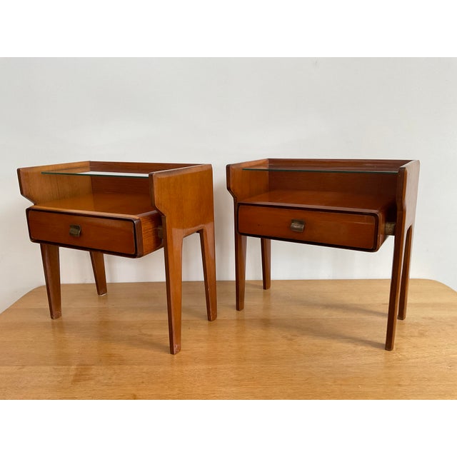 Circa 1950, mahogany veneer, upper inset glass shelf over a lower drawer with original shaped brass pull, tapered legs,...