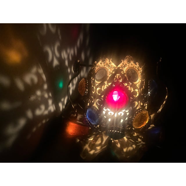 The Fairy Lamp features ornate pierced scrollwork set with large, faceted glass cabochons in various colors on a ruffled...
