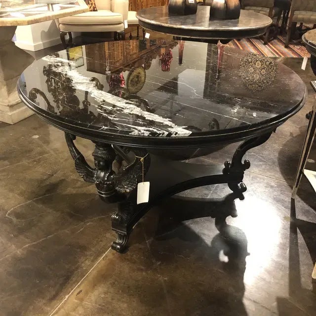 Round Empire style table with marble top on a hand carved, winged figure motif base in Vintage black finish. Created in...