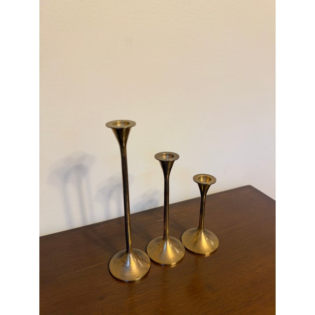 A graduated set of three mid-century modern brass candlesticks with a sleek trumpet silhouette. Each has a slender stem...