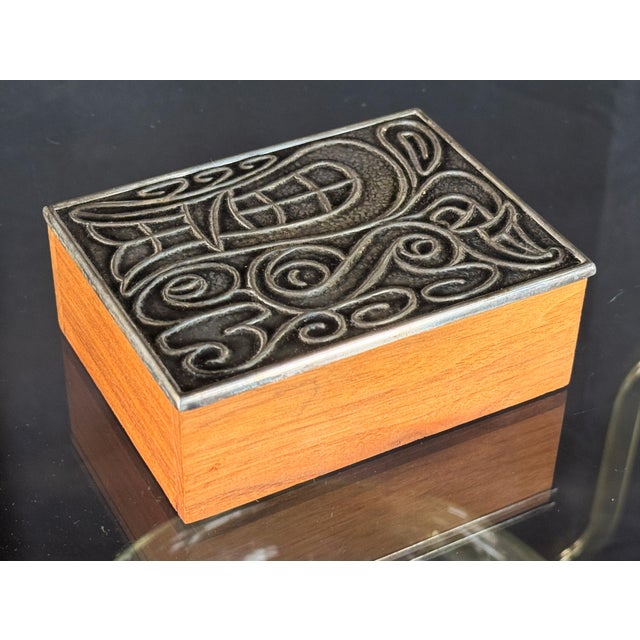 This small desktop box by Napier pairs a warm solid teak body with a fitted silverplate lid cast in an interlocking scroll...