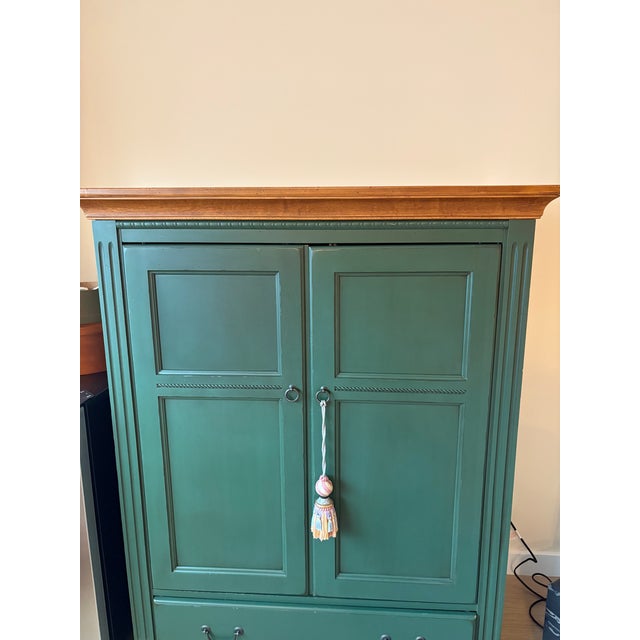Handsome painted wood armoire featuring a muted sage green finish with a contrasting natural wood crown. Paneled double...