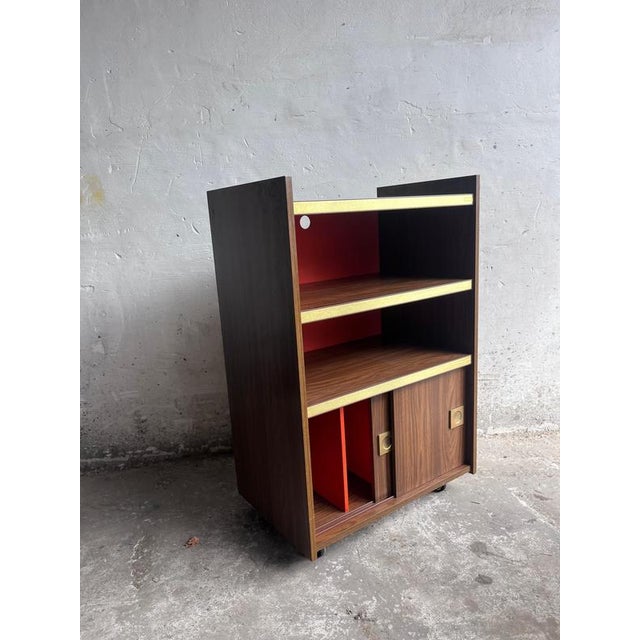 A distinctive vintage stereo cabinet dating from the 1970s. The warm wood-grain finish is contrasted by a bright red...