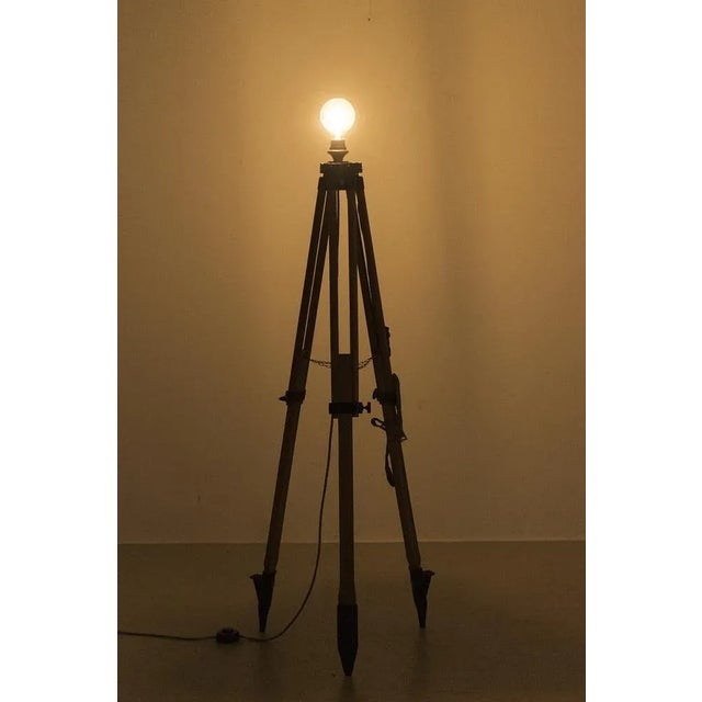 An industrial floor lamp with three legs. The base is made of a land surveying device. The floor lamp does not include a...