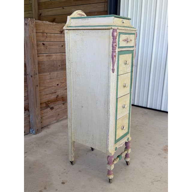 A charming vintage cottage-style tall chest featuring its original hand-painted distressed finish in soft cream, seafoam...