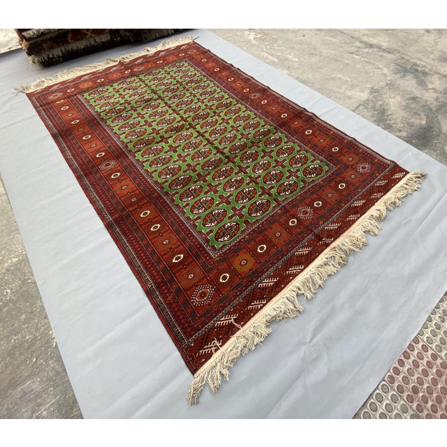 A finely hand-knotted Afghan rug featuring a rare green and rust Bukhara pattern with detailed medallions and ornate...