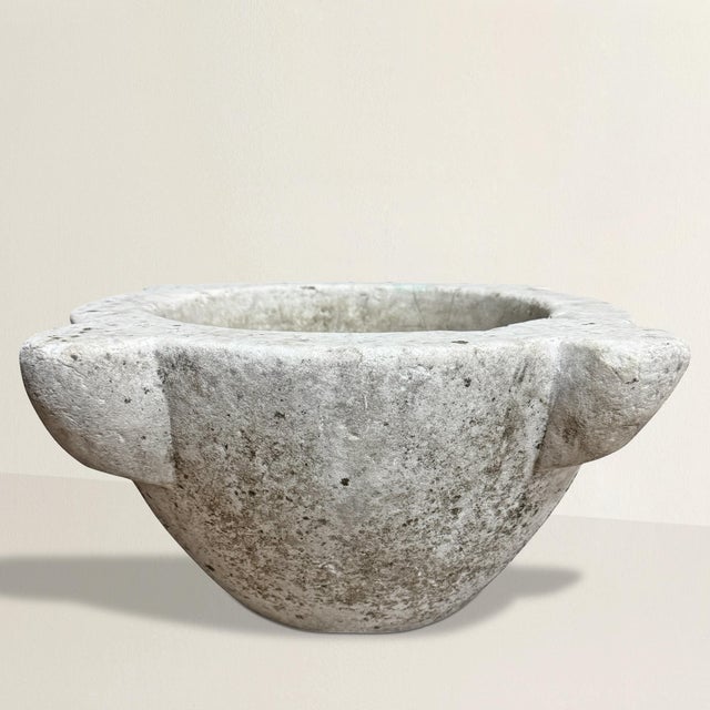 An 18th-century French carved marble mortar, rich with history and softened by centuries of use, its surface worn smooth...