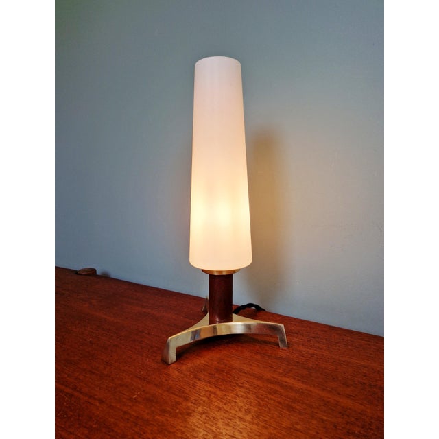 Tripod table lamp in brass and teak with a tubular shade in satin white opaline glass, Scandinavian design, 1960s. The...