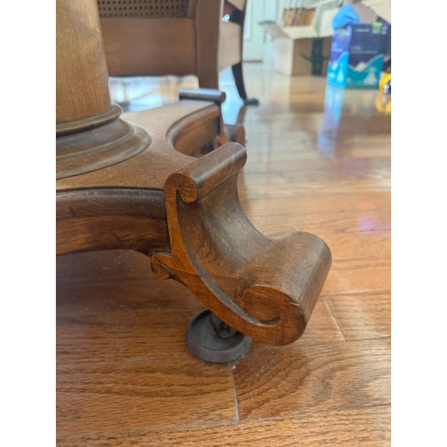 This is an oval wooden side table on a pedestal featuring an oval top with a custom glass cover and scrolled foot base...