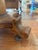 This is an oval wooden side table on a pedestal featuring an oval top with a custom glass cover and scrolled foot base...