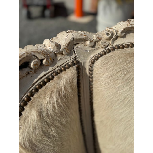 Pair of Louis XV style carved wood bergère lounge chairs featuring a distressed cream painted frame with detailed...