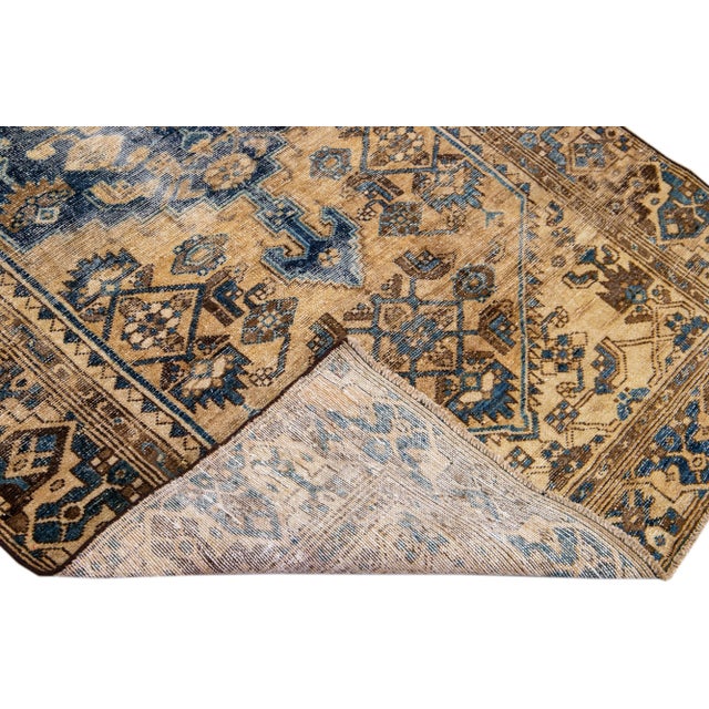Beautiful vintage Persian distressed hand-knotted wool rug with a tan color field. This piece has a beige frame and navy...