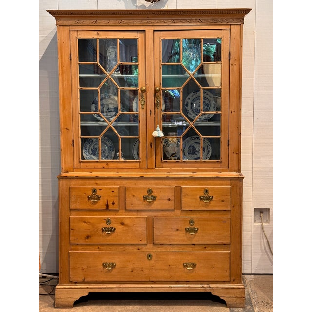 A generous country pine breakfront in one piece, with a dentil and gadrooned cornice above two glazed doors with diamond-...