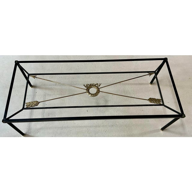 Elegant cocktail table. Iron rectangular construction with solid brass central wreath and arrows. Brass end cups on feet....