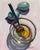 This oil painting captures a serene moment with a glass bowl containing a freshly cracked egg, accompanied by two whole...