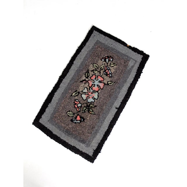 This early 20th-century antique hooked rug features a bold black and gray background with a red and blue floral design,...