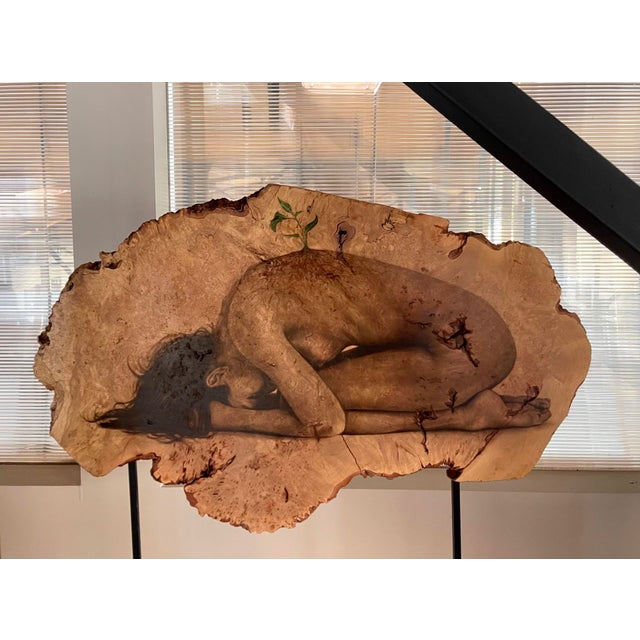 This artwork features a deeply introspective figure curled in a fetal position, seamlessly integrated into the natural...