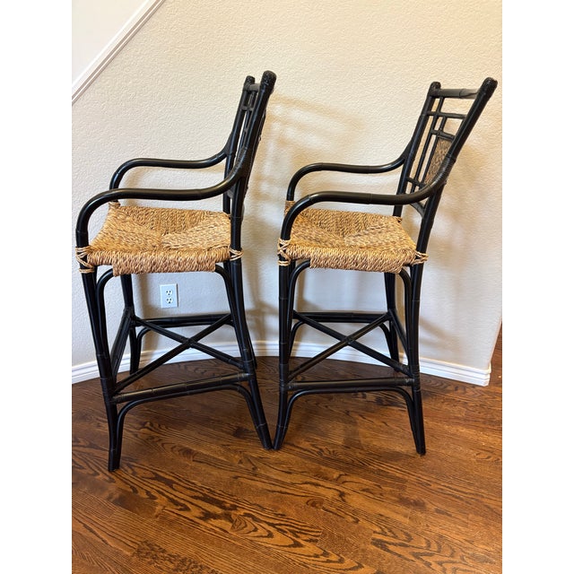 A fabulous pair of Hollywood Regency–style Chinoiserie barstools featuring glossy black lacquered bamboo frames,...