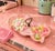 A vintage, ceramic pottery dish, in the form of overlapping leaves, with pink glaze, gold details, and a metal carrying...