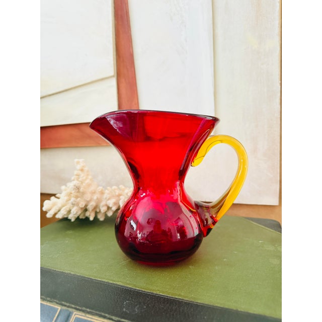 This striking vintage art glass pitcher is attributed to Blenko and features a rich ruby red body paired with a...