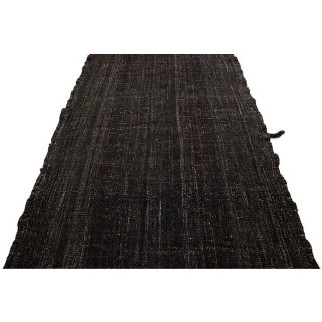 The Deco flatweave wool runner displays a striking dark brown color scheme, contributing to a modern and visually...