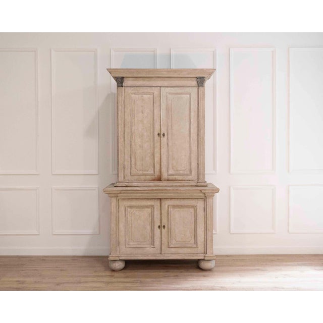 A substantial, two‑piece Swedish cabinet in a light grey wash with white highlights, dating to roughly 1820–1850. Each...