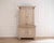 A substantial, two‑piece Swedish cabinet in a light grey wash with white highlights, dating to roughly 1820–1850. Each...