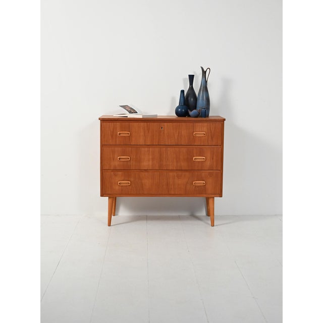 1950s–1960s teak chest of drawers with oak details: three drawers with double recessed handles and tapered turned legs....
