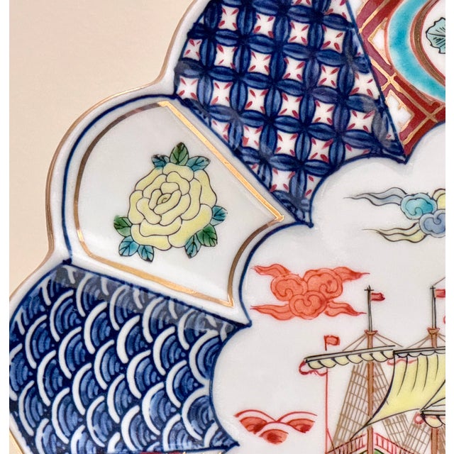 A vintage Japanese hand-painted porcelain plate in an Imari-inspired style, featuring a richly detailed central scene of a...