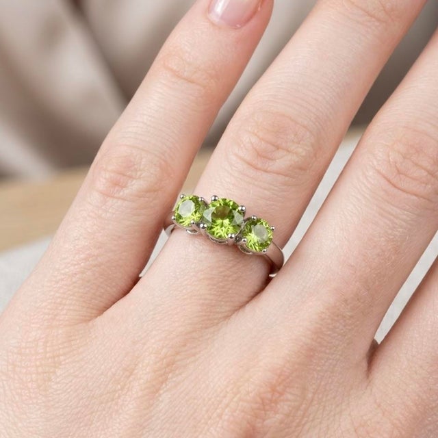 This captivating ring features three round-cut peridot gemstones, each radiating a vibrant green hue that symbolizes...