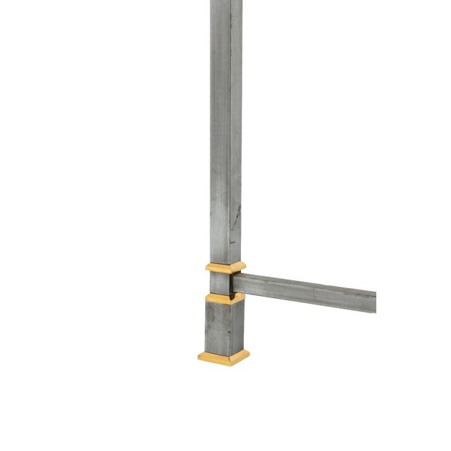 A circular table in brushed and gilt metal and standing on four square legs, with gilt rings and linked between them by a...