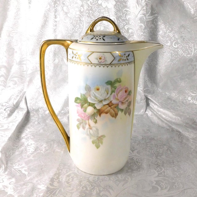 This is a Royal Rudolstadt porcelain coffee pot in an unknown pattern. The pot is white with a pale peach and white rose...