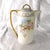 This is a Royal Rudolstadt porcelain coffee pot in an unknown pattern. The pot is white with a pale peach and white rose...
